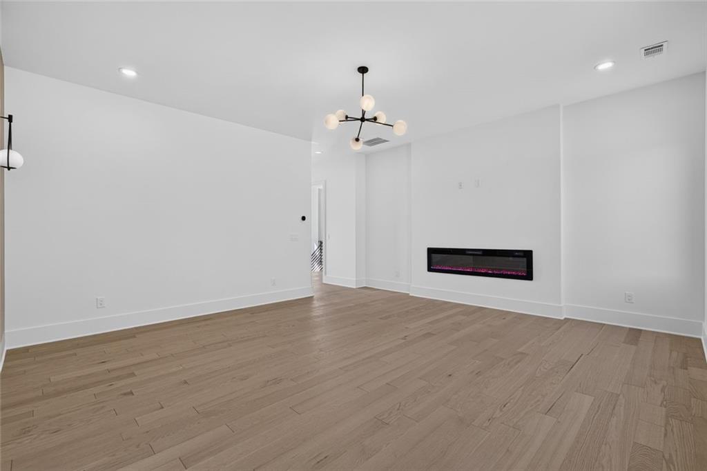Unfurnished living room with light wood floors, a globe chandelier, and a linear electric fireplace.