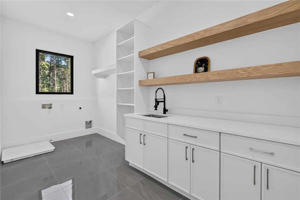 Modern laundry room with white cabinets, open wood shelves, and a window overlooking trees.