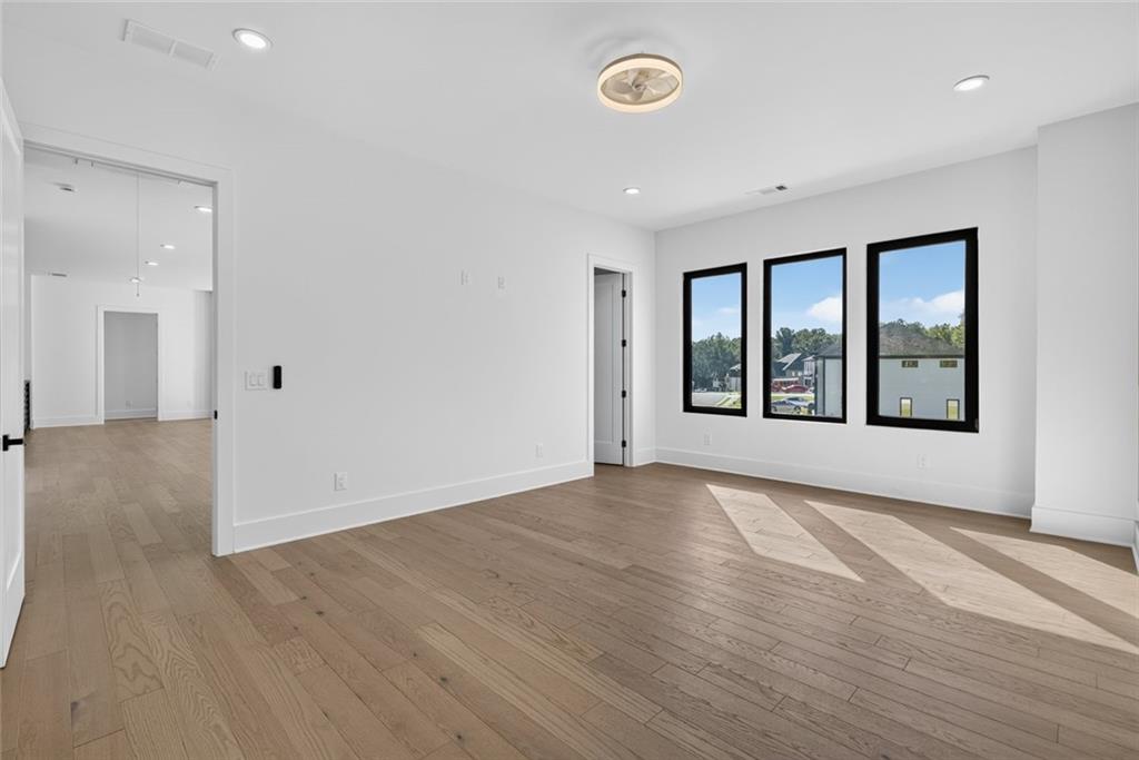 Vacant room with light wood floors, three tall windows, and sunlight stretching across the floor.