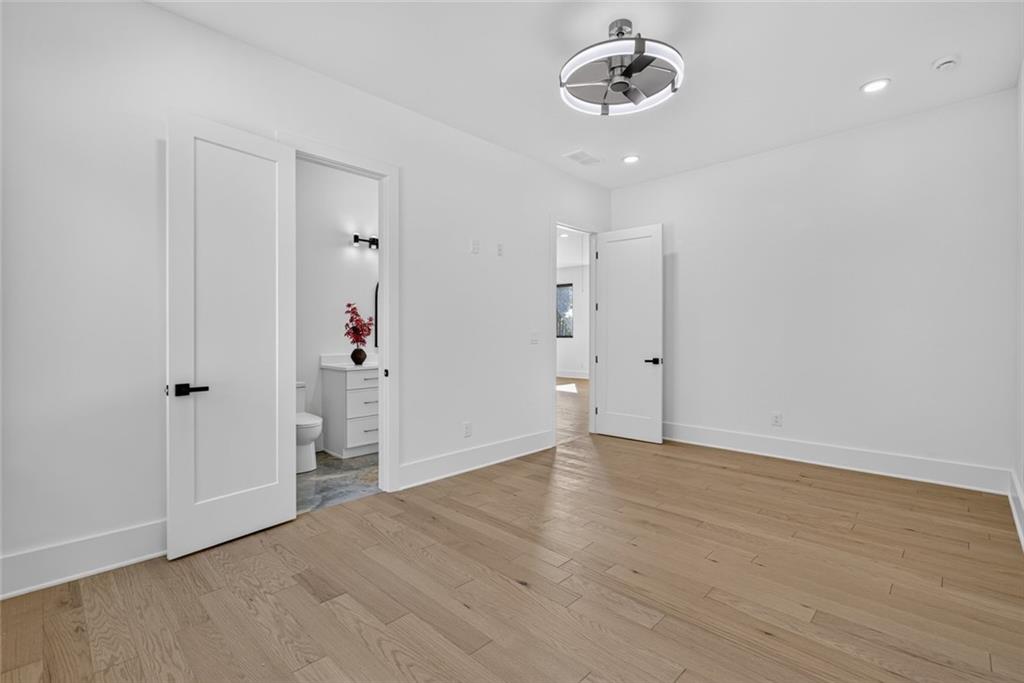 Empty bedroom with light wood floors, a modern ceiling fan, and an open doorway to the bathroom.
