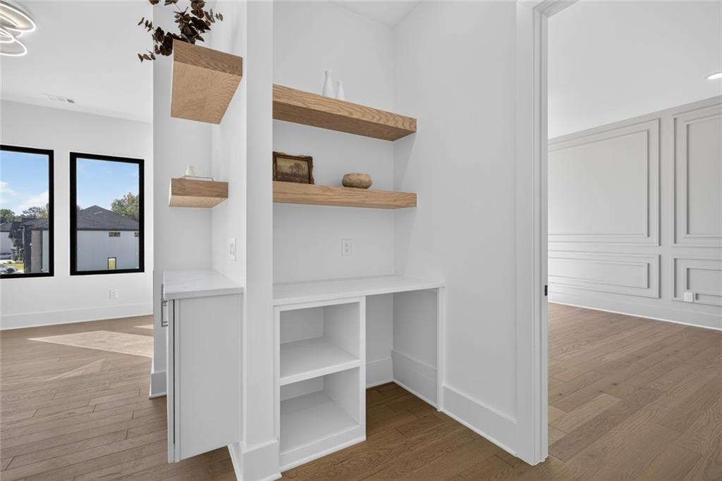 Built-in office nook with open wood shelves and a countertop desk beside hardwood-floored rooms.