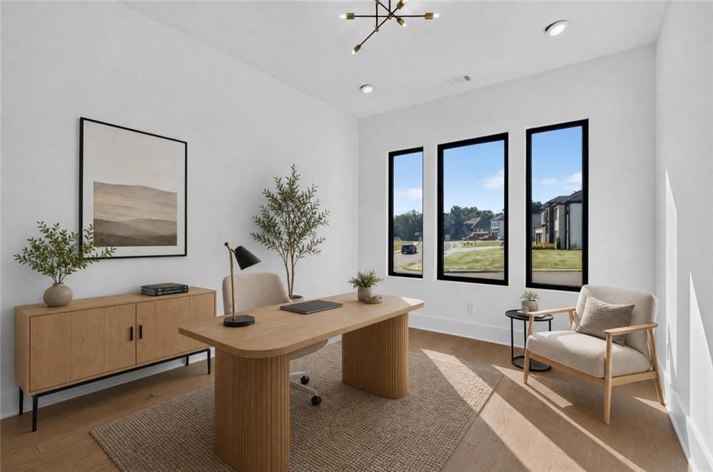 Home office with a sculptural wood desk, three tall windows, and a lounge chair.