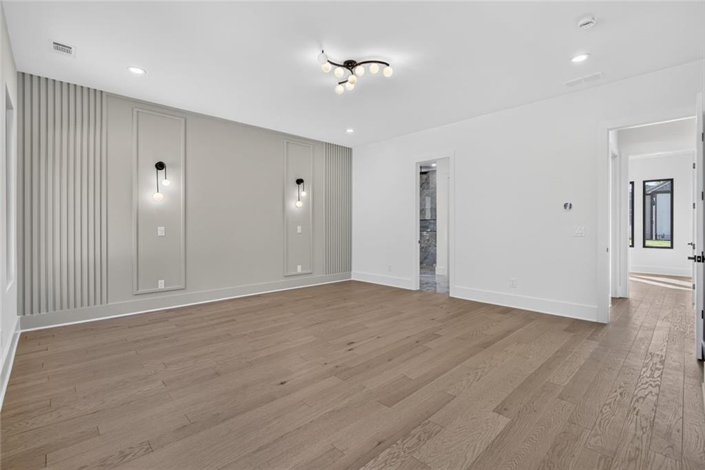 Unfurnished room with wide-plank wood floors and a gray slatted accent wall with wall sconces.