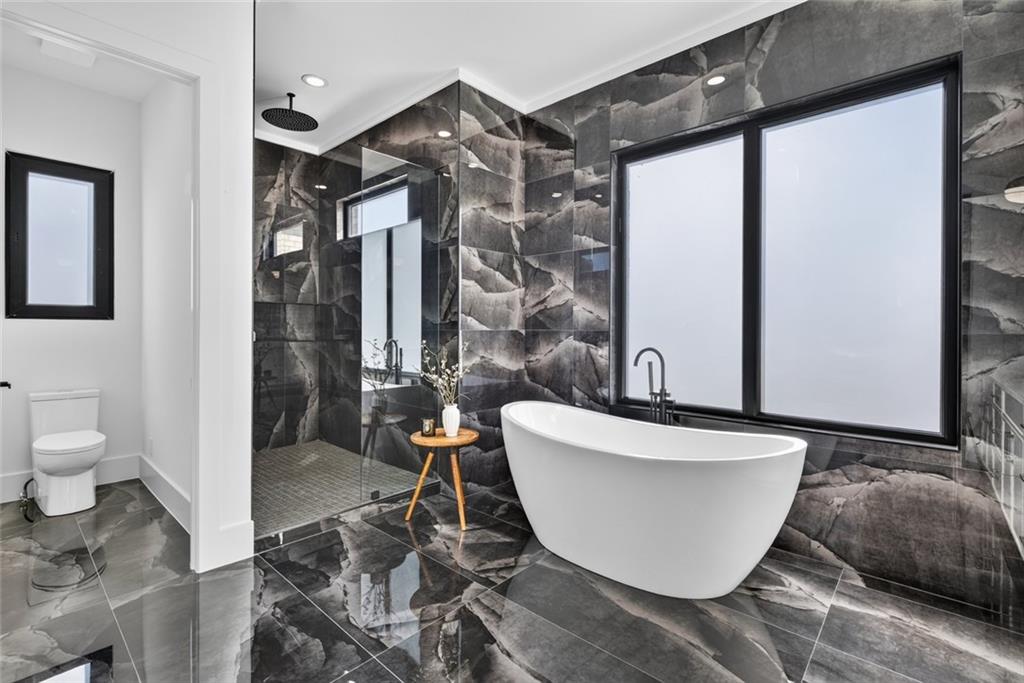 Modern bathroom with a freestanding tub, dark marble-look tile, large windows, and glass-enclosed shower.