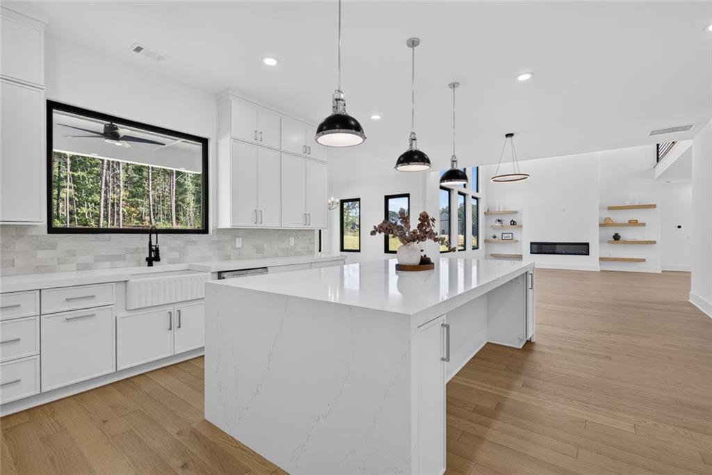 Modern white kitchen with a waterfall-edge island, pendant lights, and windows overlooking trees.