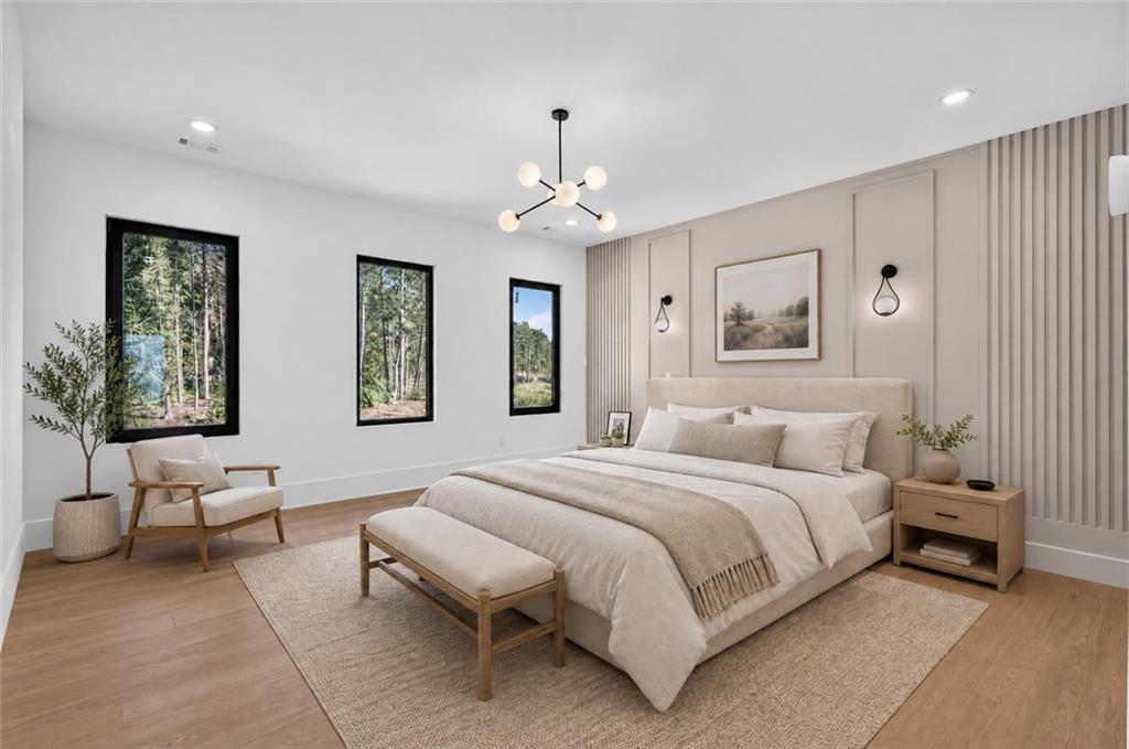 Staged bedroom with a large upholstered bed, neutral bedding, and three tall windows overlooking trees.