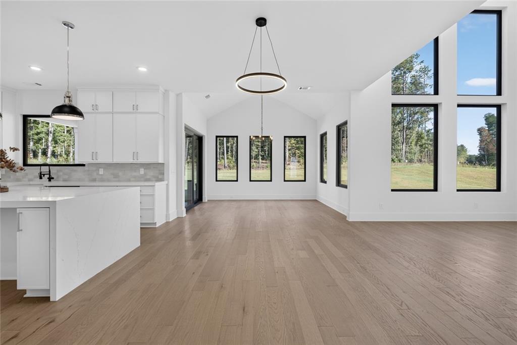 Open-plan kitchen and living area with a large island, vaulted ceiling, and tall windows overlooking trees.