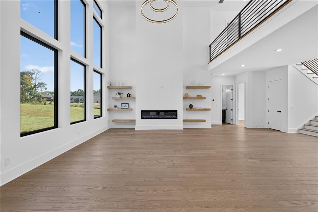 Unfurnished living room with tall windows, a linear fireplace, floating shelves, and an open upper-level railing.