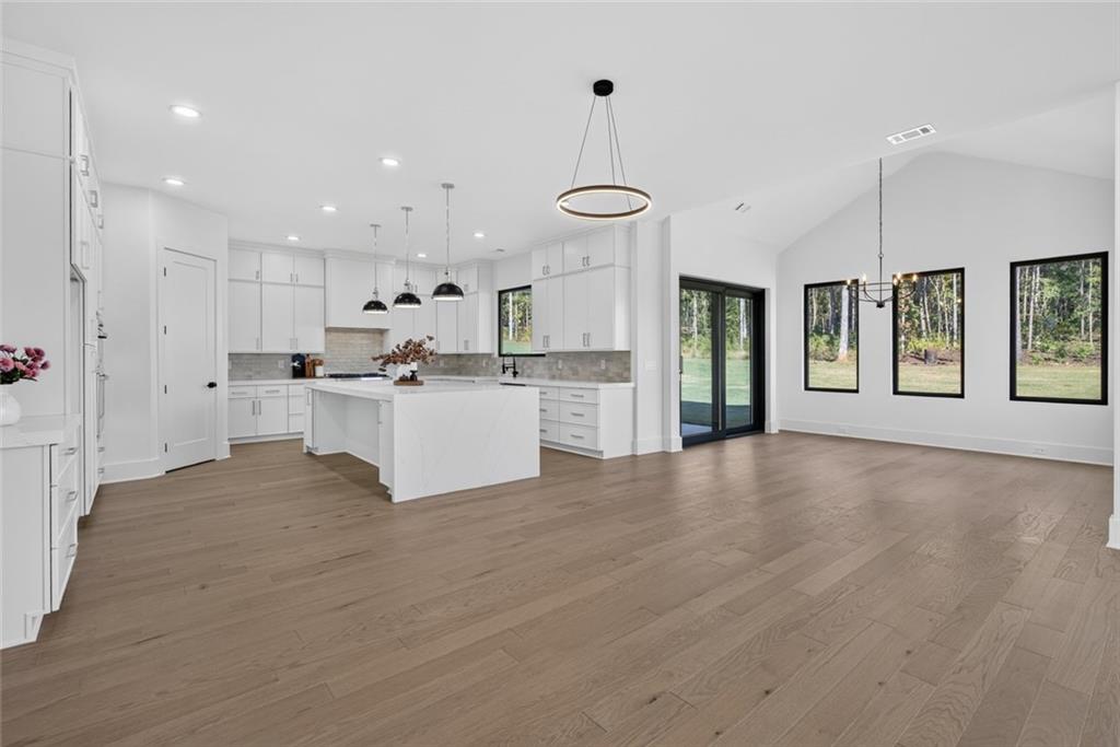 Open-plan kitchen and living area with a white island, light wood floors, and black-framed windows.