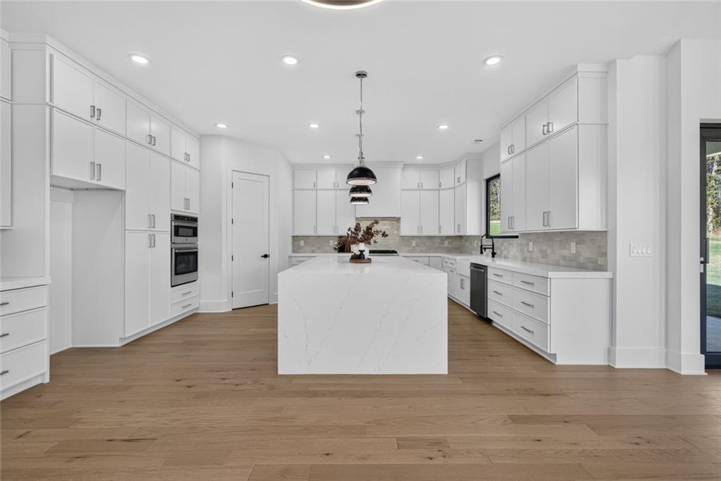 Modern white kitchen with a large island, light wood floors, and black pendant lights.