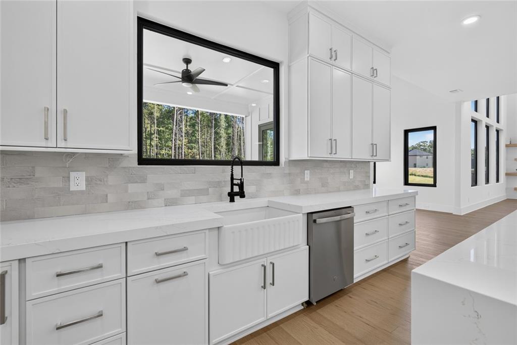 Modern white kitchen with an apron-front sink, black faucet, and large window overlooking trees.