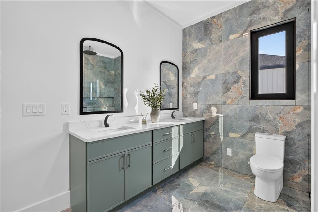 Modern bathroom with a sage-green double vanity, arched mirrors, and gray stone-look tile.