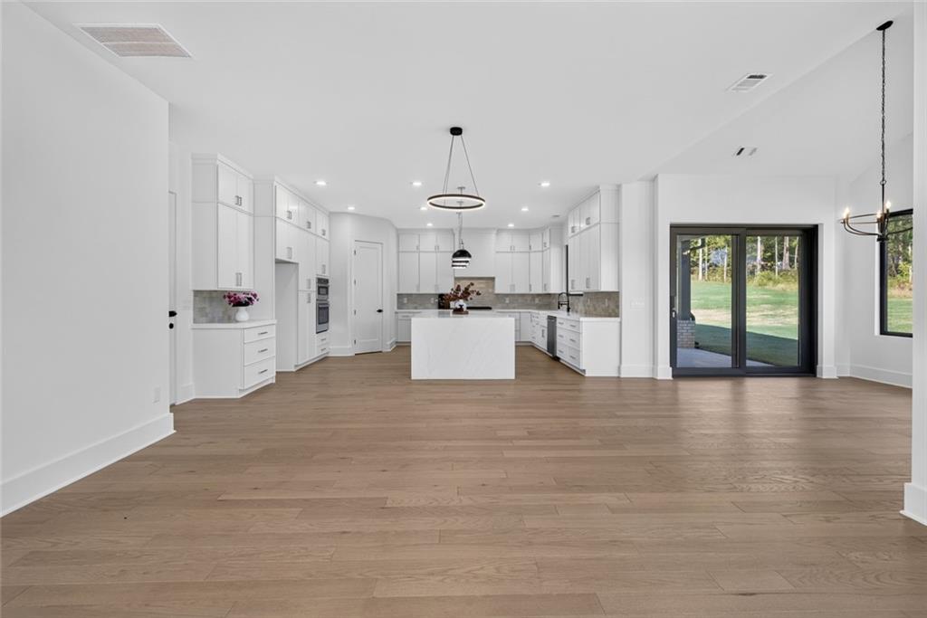 Bright vacant kitchen with white cabinetry, a central island, and wide-plank wood flooring.