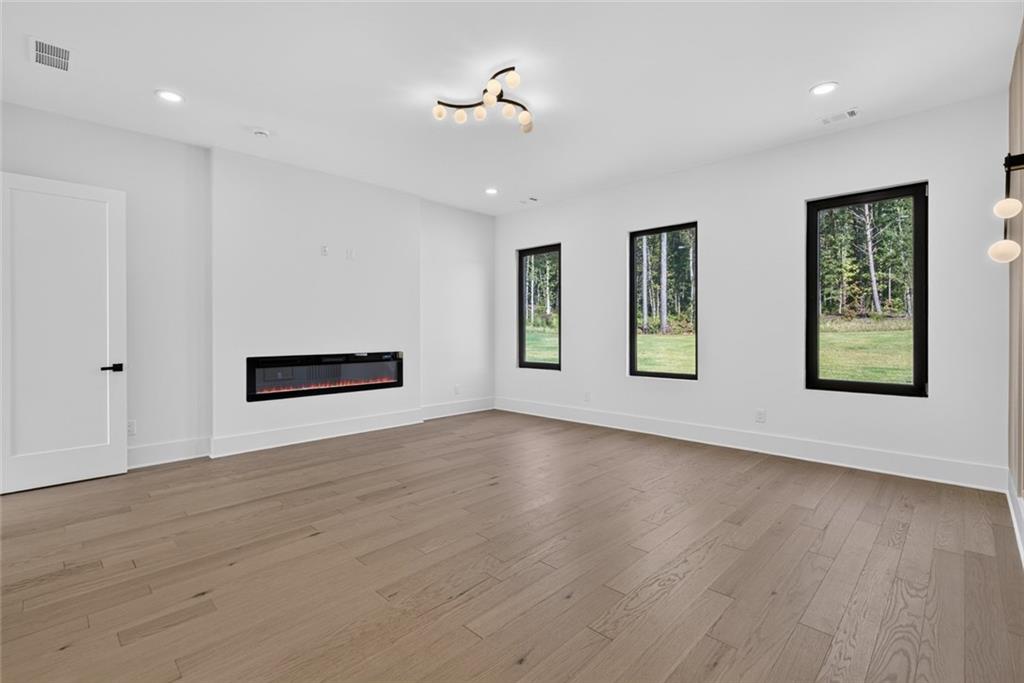 Unfurnished living room with a linear fireplace, wood flooring, and windows overlooking trees.