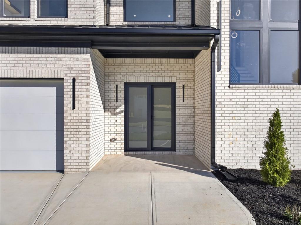 White-brick home entrance with covered porch, dark-framed glass doors, and garage.