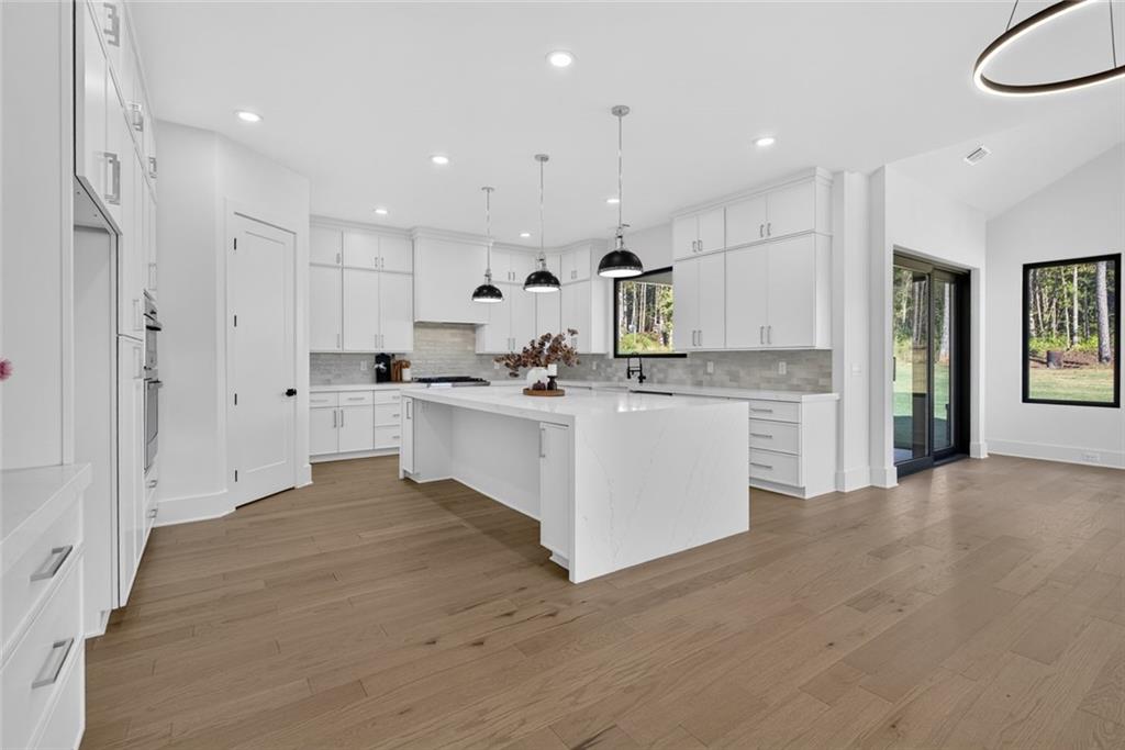 Modern white kitchen with a large waterfall island, pendant lights, and views of trees.