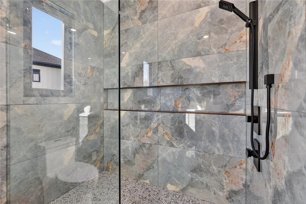 Bathroom shower with veined gray tile, frameless glass enclosure, black fixtures, and mosaic floor.