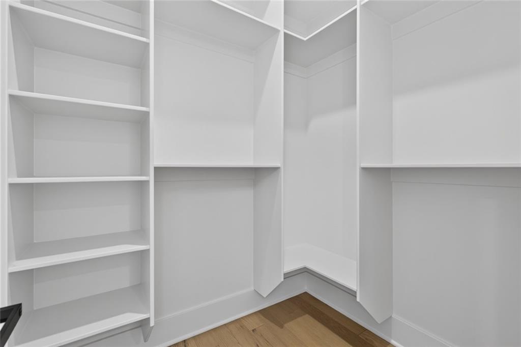 Walk-in closet with white built-in shelving and a light wood floor.
