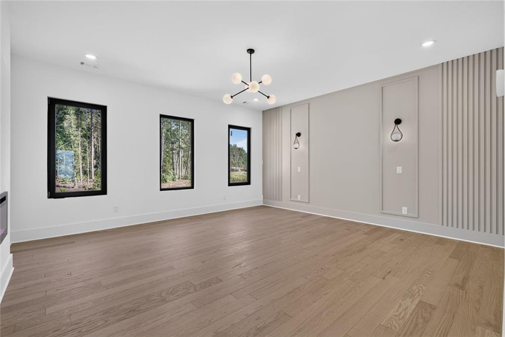 Empty dining room with three black-framed windows, wood floors, and a paneled accent wall.