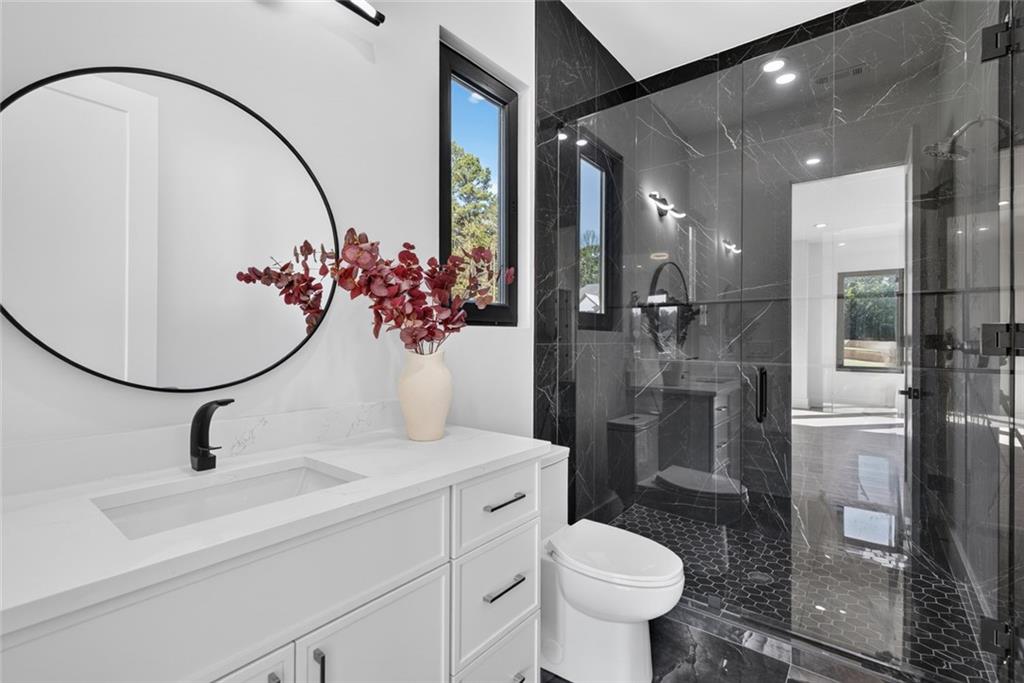 Modern bathroom with a white vanity and a glass shower clad in dark marble.