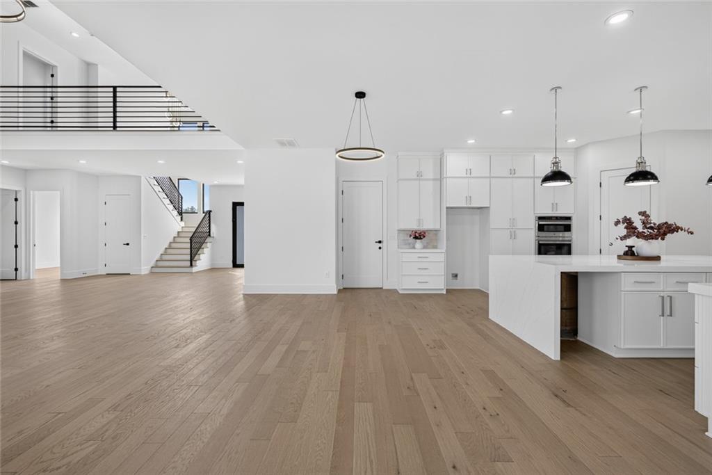 Open-plan kitchen with a large white island, light wood floors, and a staircase with dark railing.