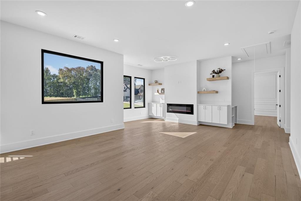 Unfurnished living room with wide-plank wood floors, large windows, and a built-in linear fireplace.