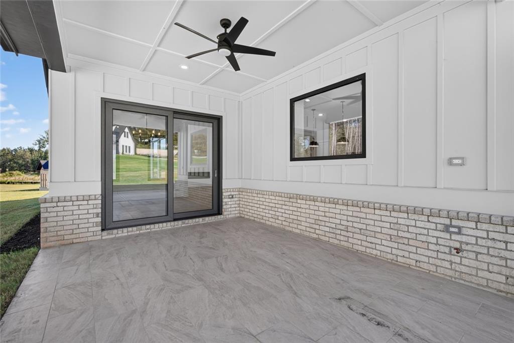 Covered patio with gray tile, brick wainscoting, and sliding glass doors overlooking a lawn.