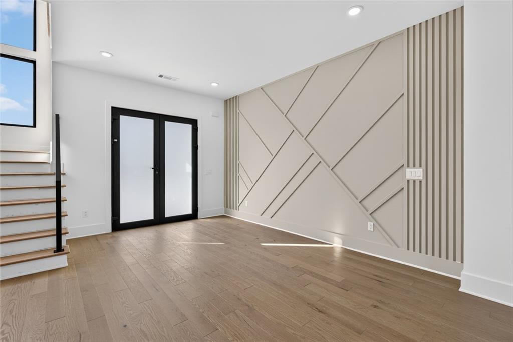 Unfurnished living room with a geometric accent wall, black-framed doors, and a staircase.