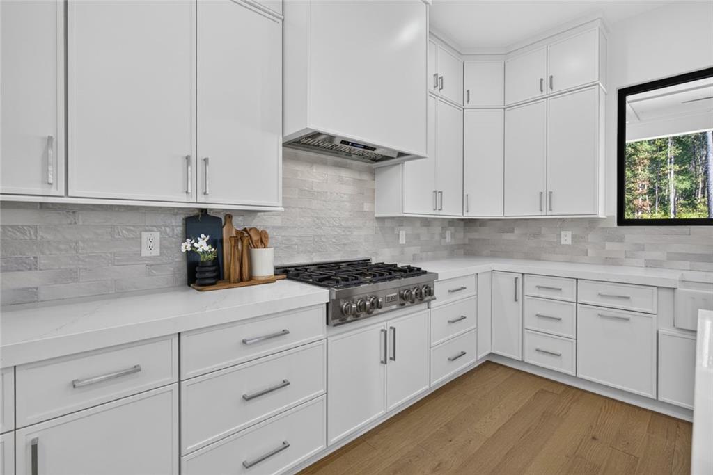 White kitchen with a stainless steel gas range, stone backsplash, and wood flooring.