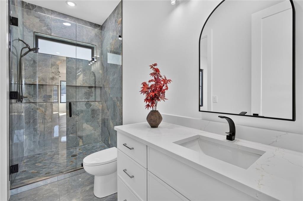 Modern bathroom with a white vanity, arched mirror, and glass-enclosed gray stone shower.