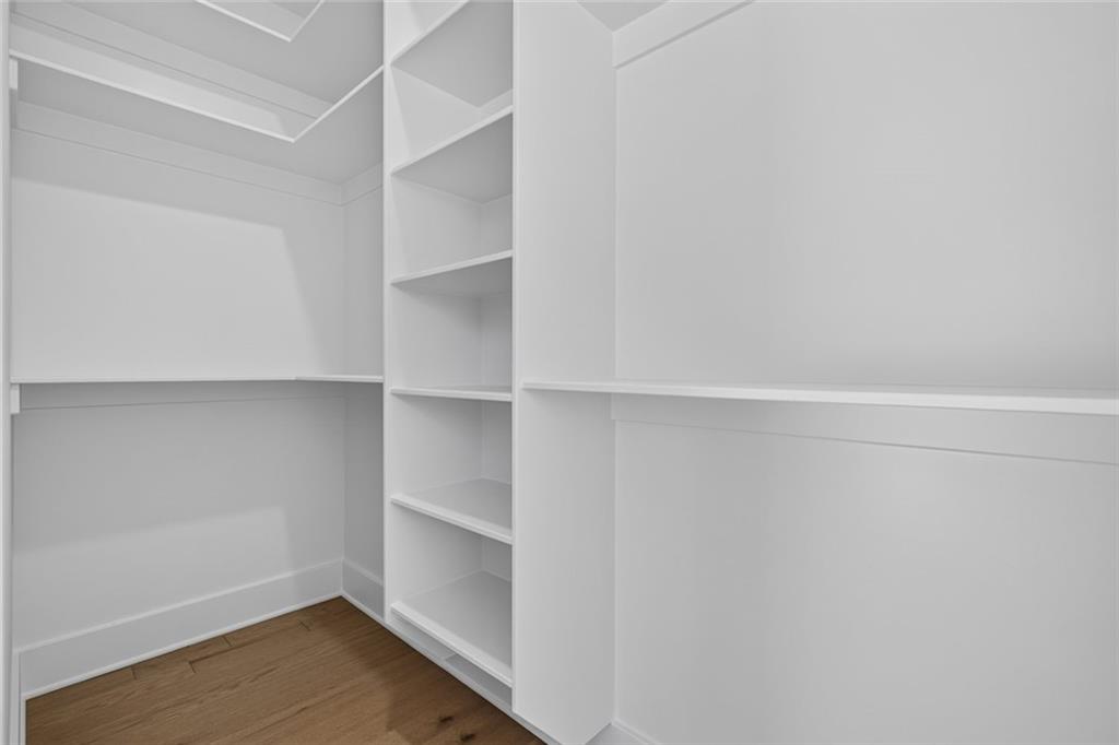 Walk-in closet with white built-in shelving and a wood floor.