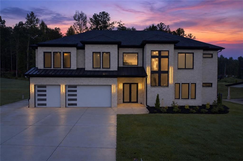 Two-story white-brick home with a two-car garage and tall black-framed windows at dusk.