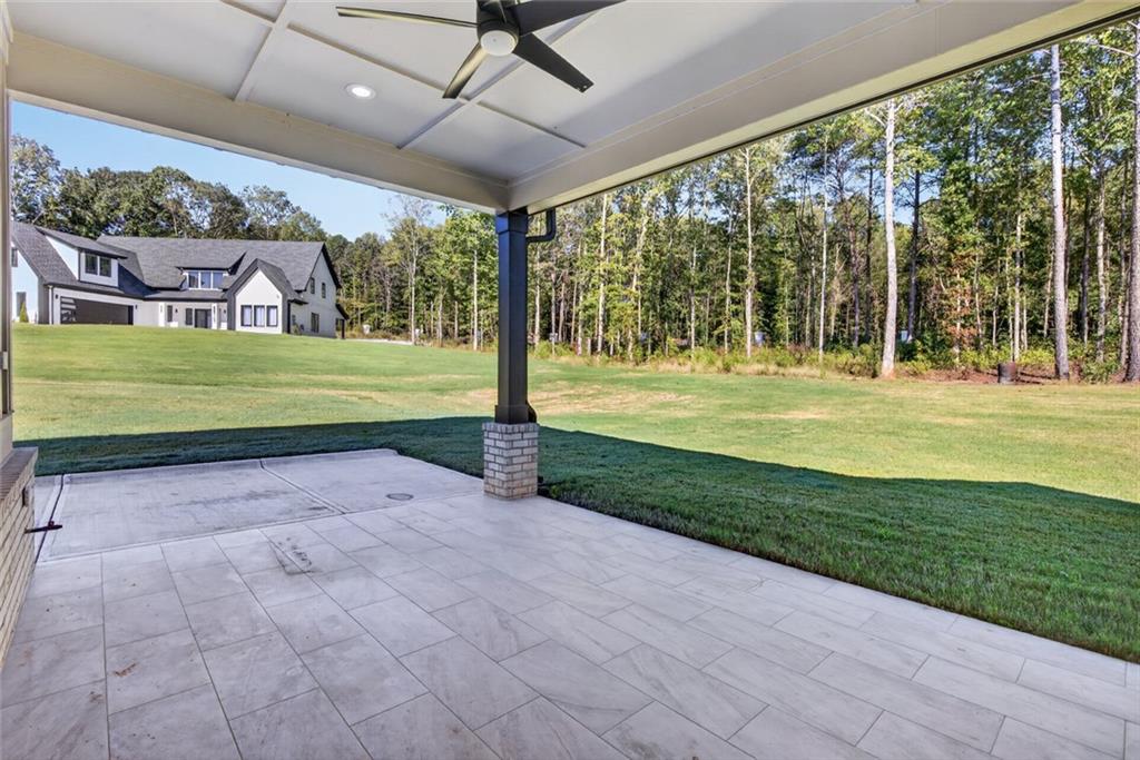Covered tiled patio overlooking a green lawn and wooded yard, with the home visible beyond.