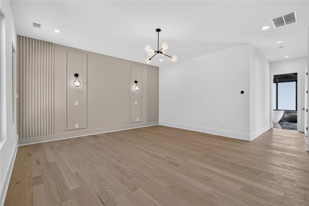 Empty bedroom with a paneled accent wall, wood flooring, and an adjoining bathroom.