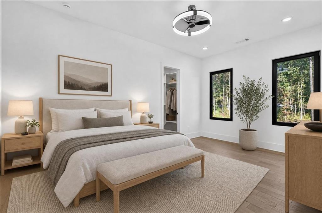 Staged bedroom with a king-size bed, upholstered bench, ceiling fan, and windows overlooking trees.
