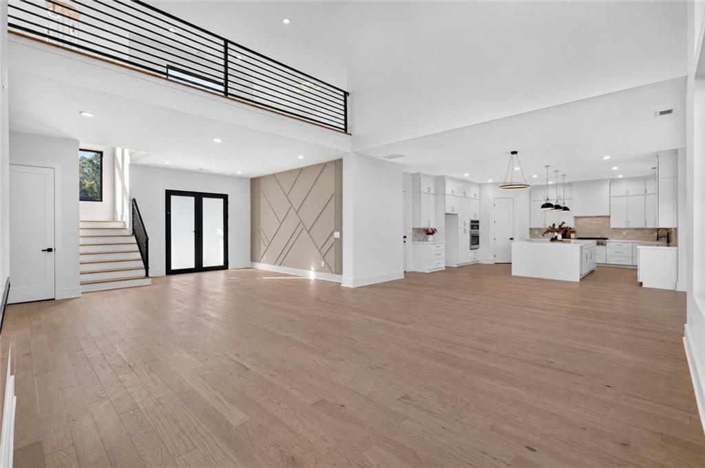 Open-plan living area and white kitchen with light wood floors, staircase, and loft railing.