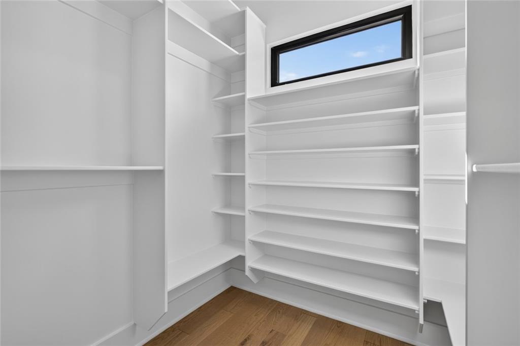 Walk-in closet with built-in white shelving, a high window, and hardwood flooring.