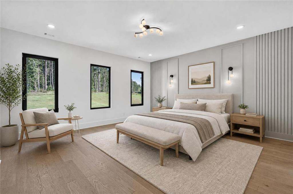 Staged bedroom with a king bed, upholstered bench, and tall windows overlooking trees.