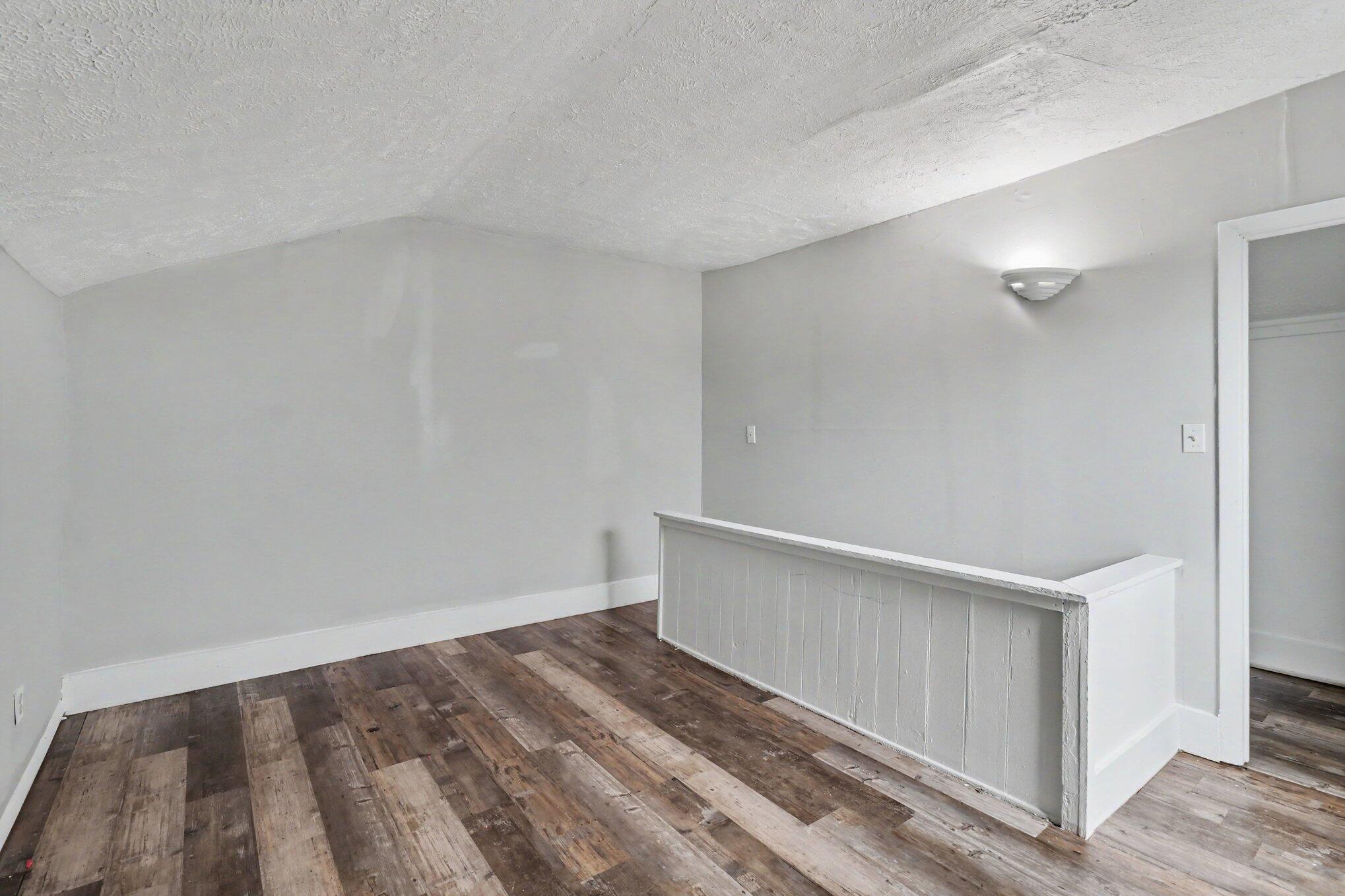 Vacant interior with dark plank flooring and a white half-wall railing.