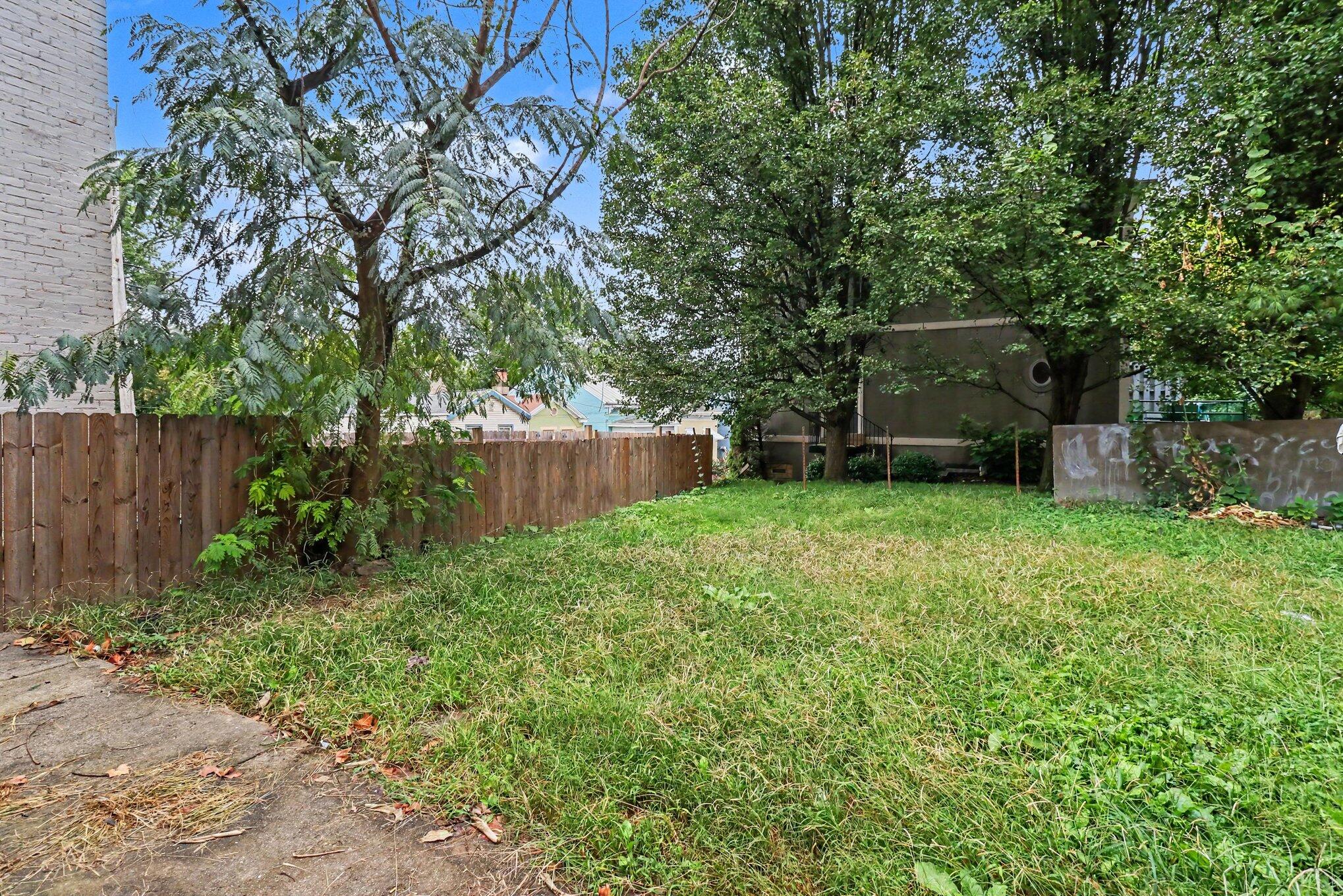 Grassy backyard shaded by mature trees, with a wooden fence and concrete walkway.