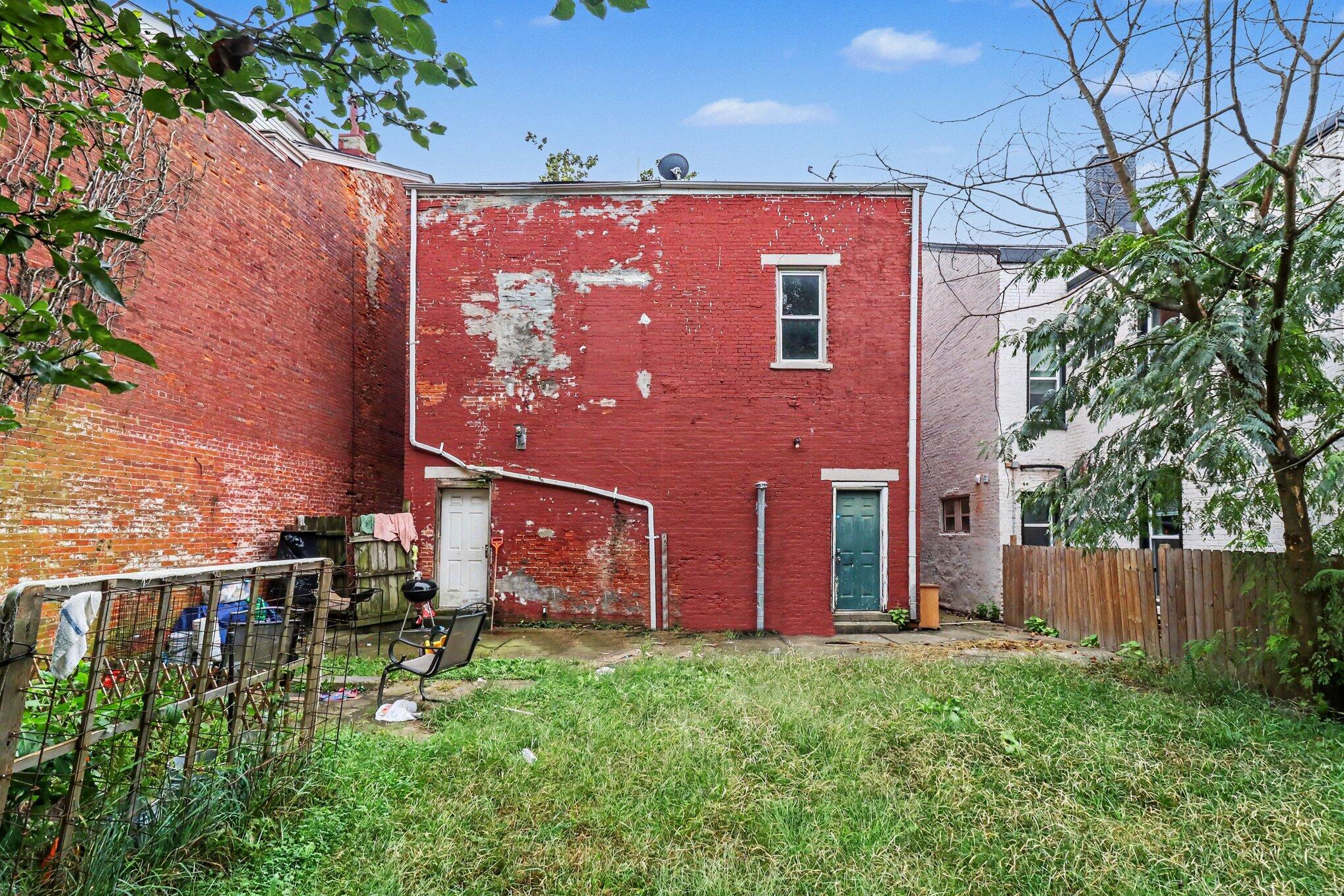 Rear of a red brick building with peeling paint, two doors, and a grassy yard.