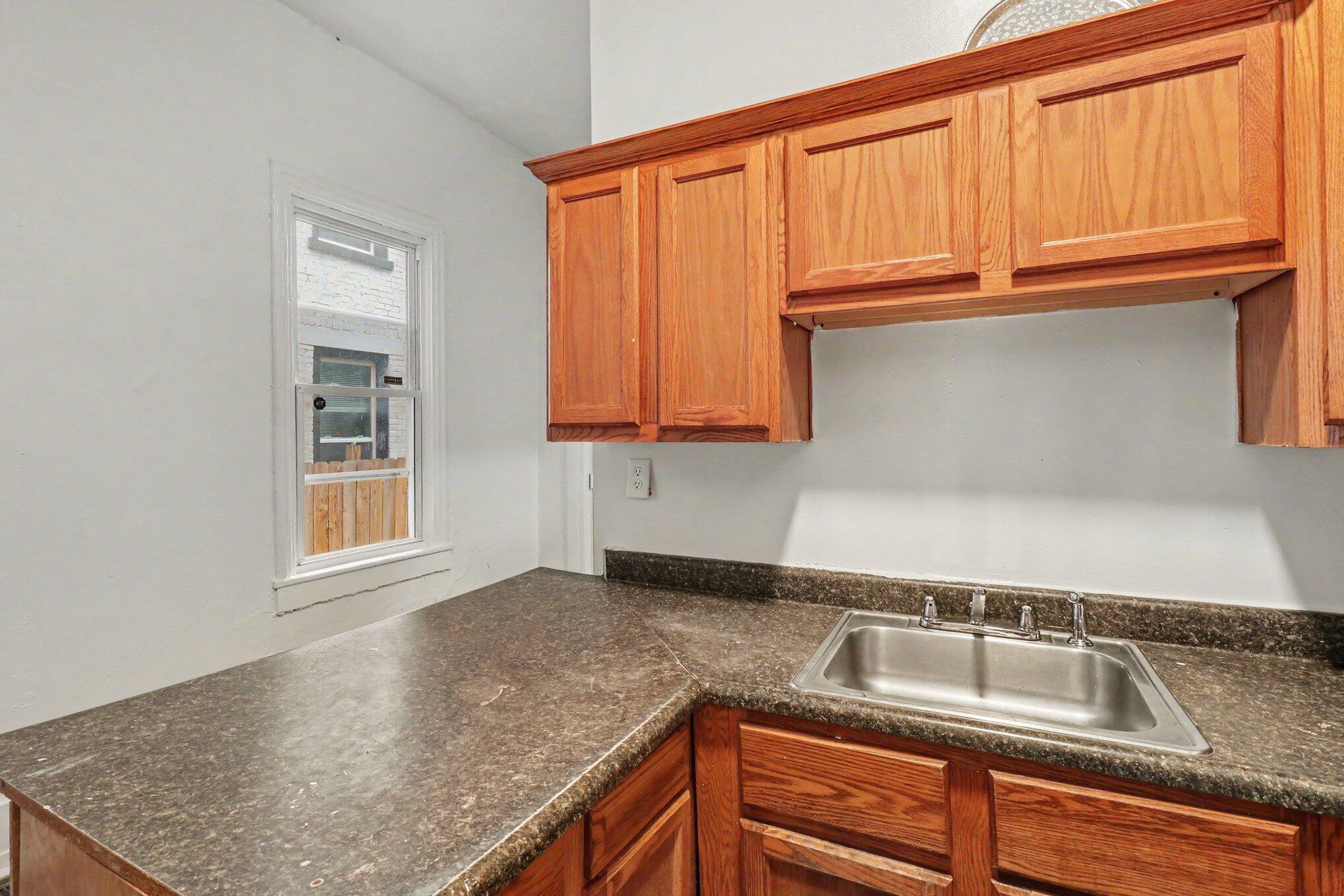 Kitchen with warm wood cabinets, dark counters, and a stainless-steel sink beneath upper cabinets.