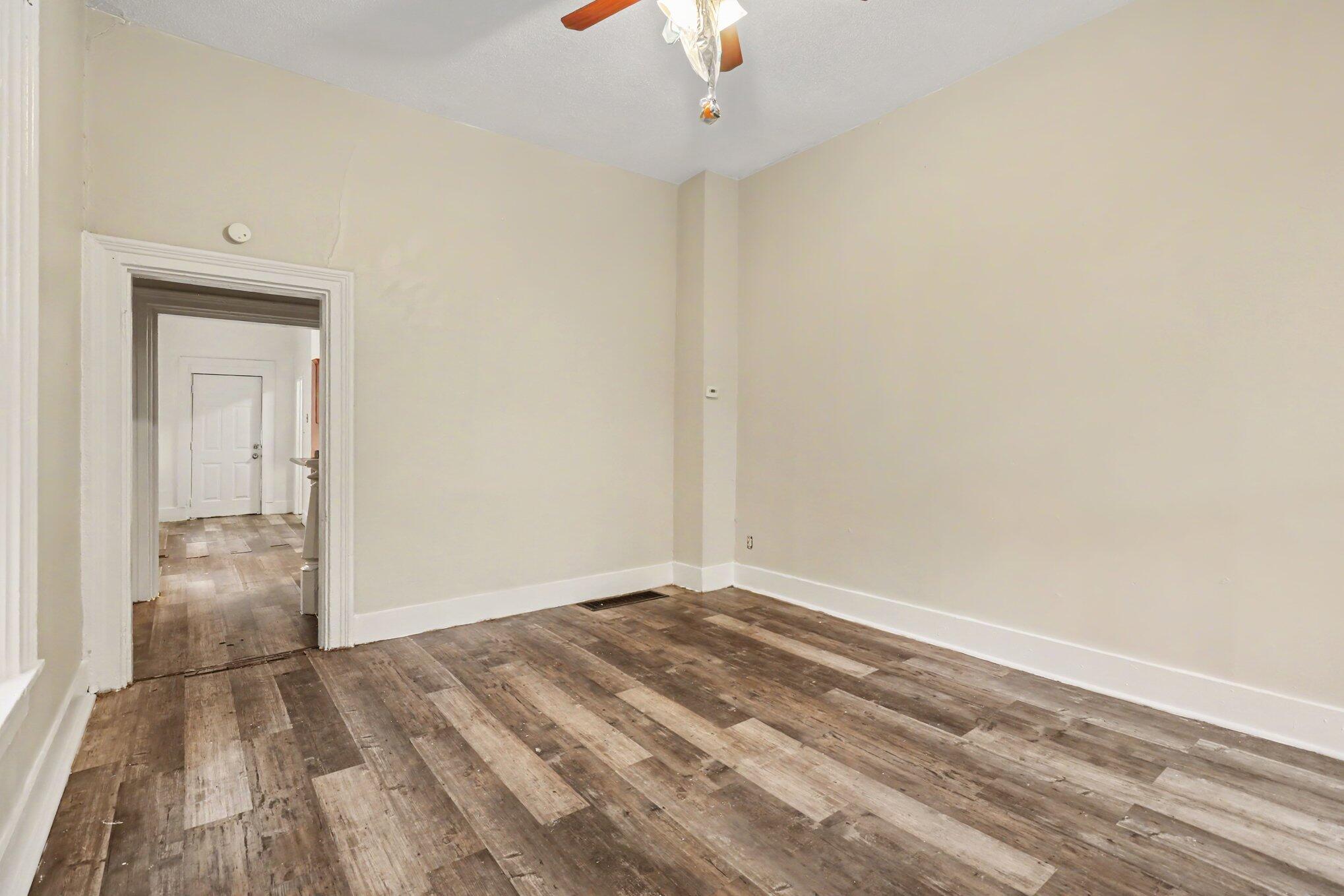Empty room with distressed-look wood flooring, beige walls, and an open doorway to the hall.