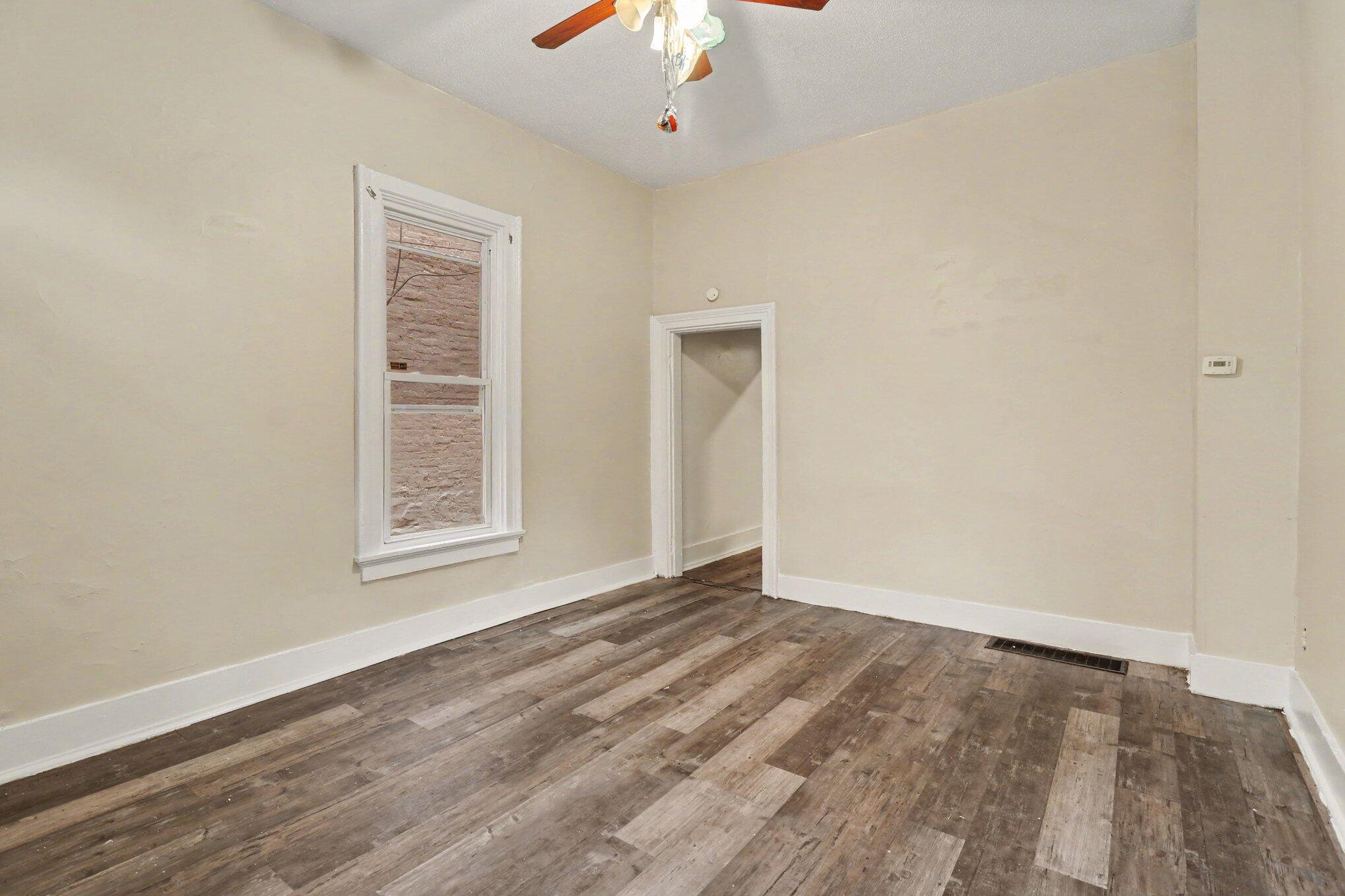 Empty room with beige walls, a white-trimmed window, and wood plank flooring.