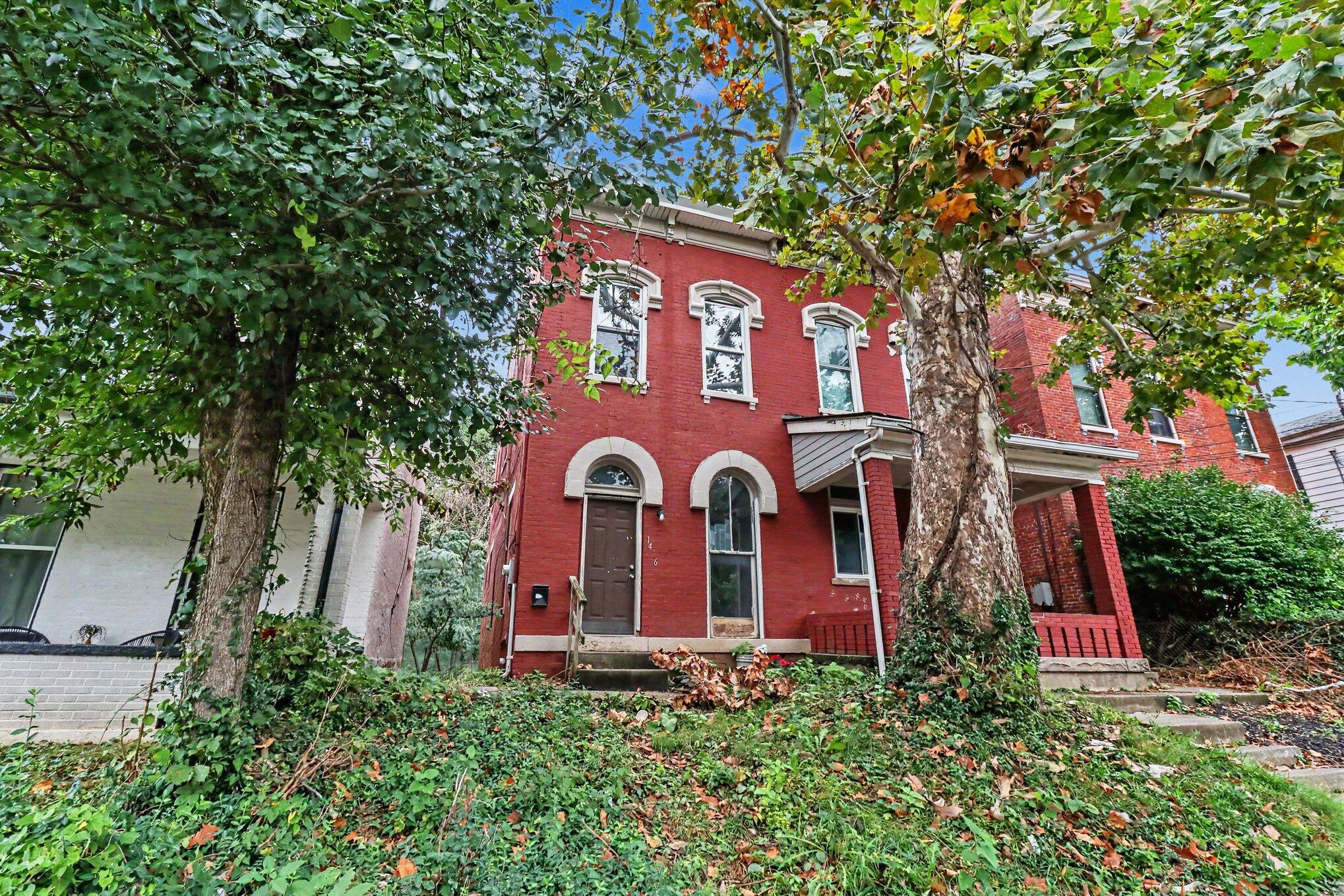 Red brick home with arched windows and a covered porch, framed by large trees and autumn foliage.