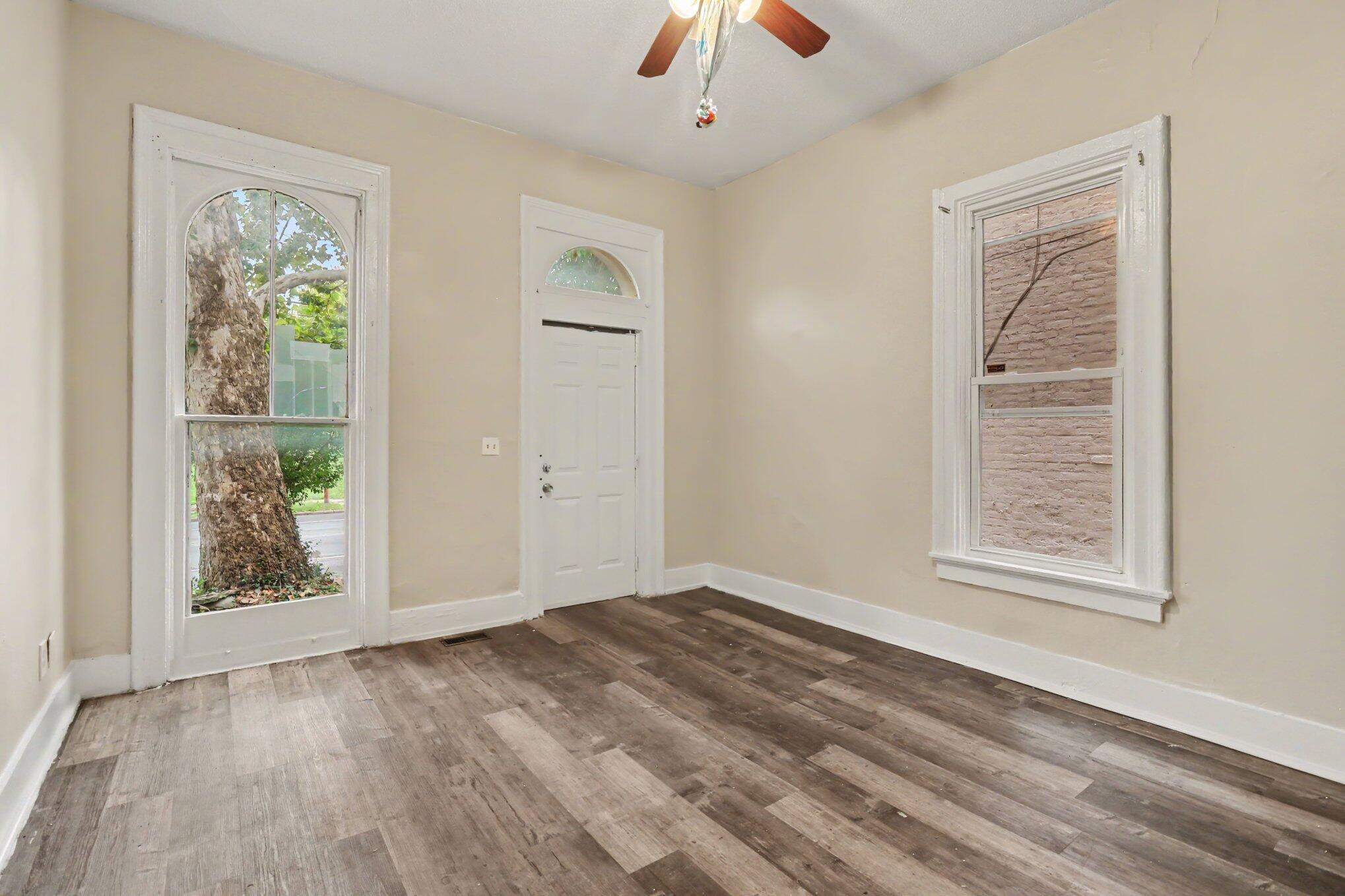 Empty entry room with wood-look flooring, an arched front-door window, and two tall windows.
