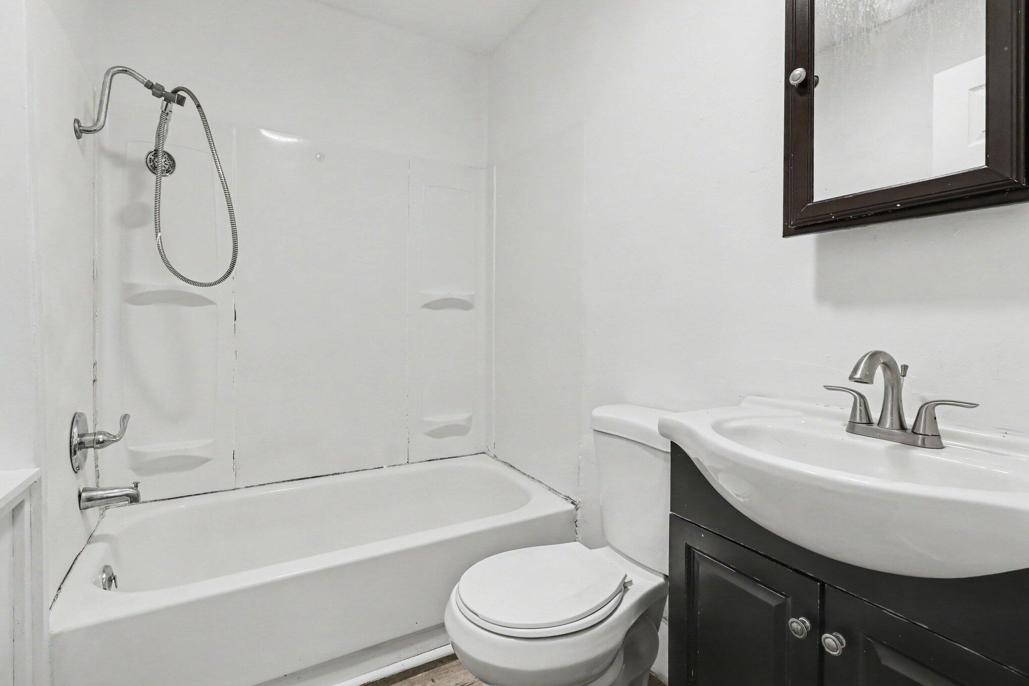 Bathroom with a white tub and shower, toilet, and sink on a dark vanity.