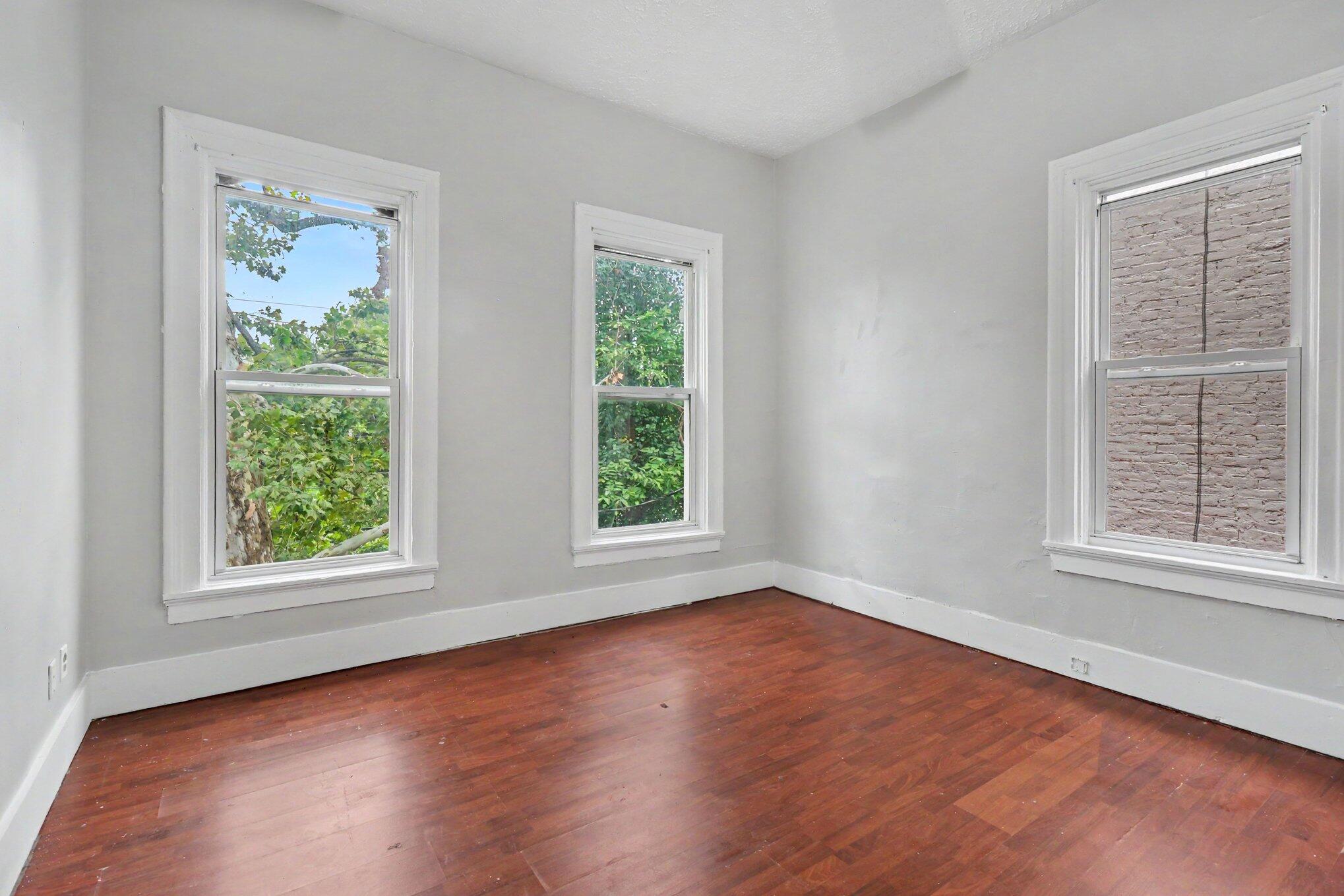 Empty room with reddish-brown hardwood floors and three white-trimmed windows.
