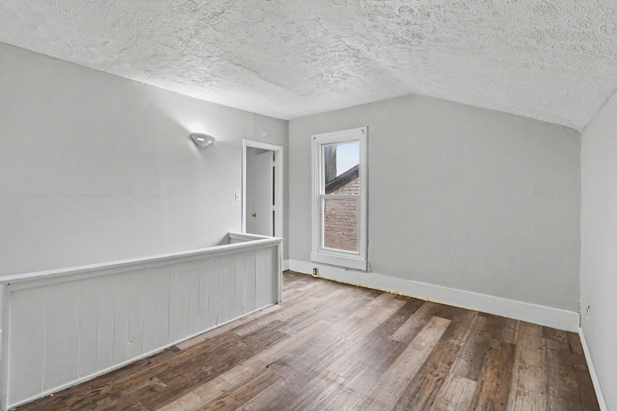 Vacant upstairs room with a sloped ceiling, mixed-tone plank flooring, and a white half-wall railing.