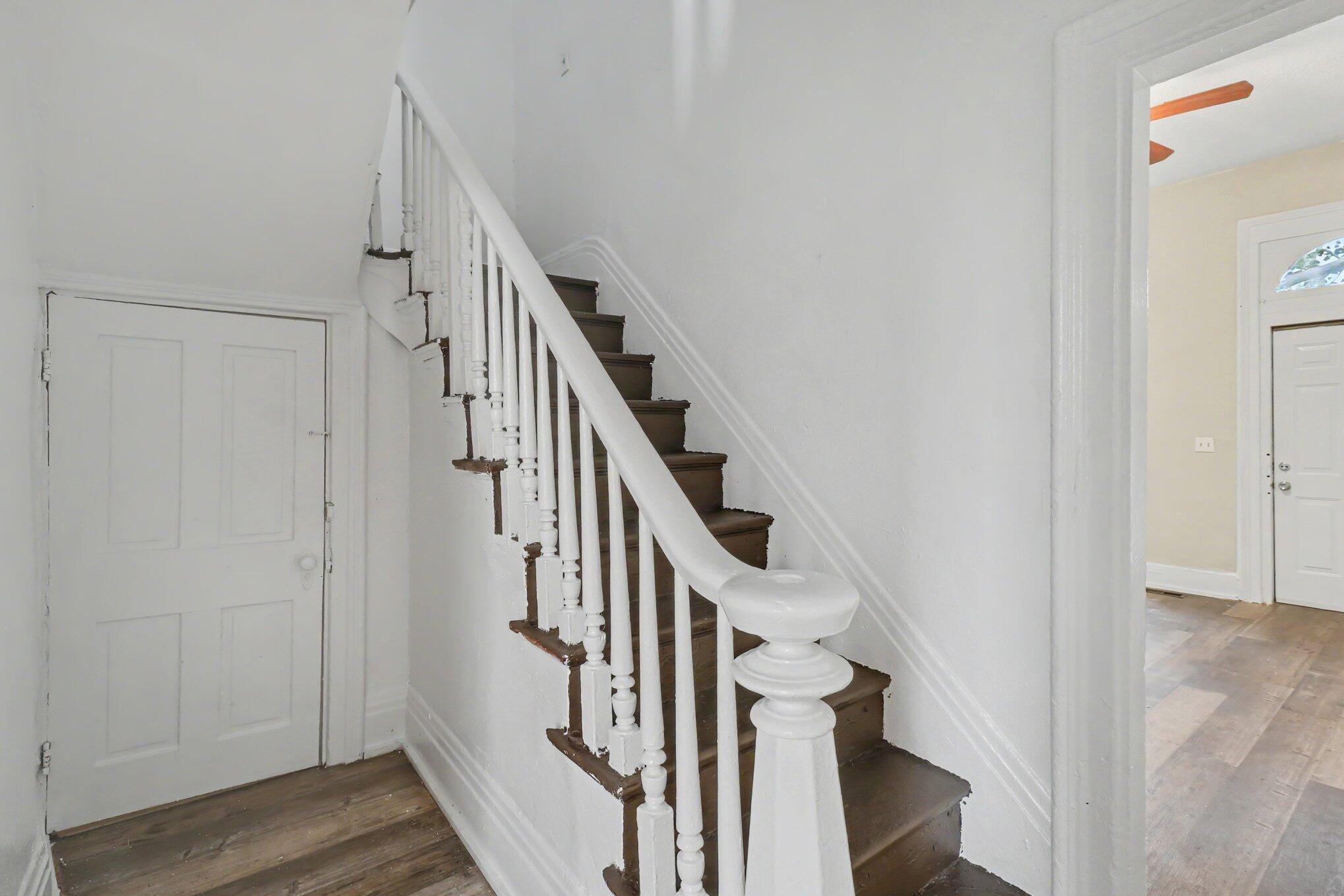 Dark wood staircase with white balusters beside a paneled door beneath the stairs.